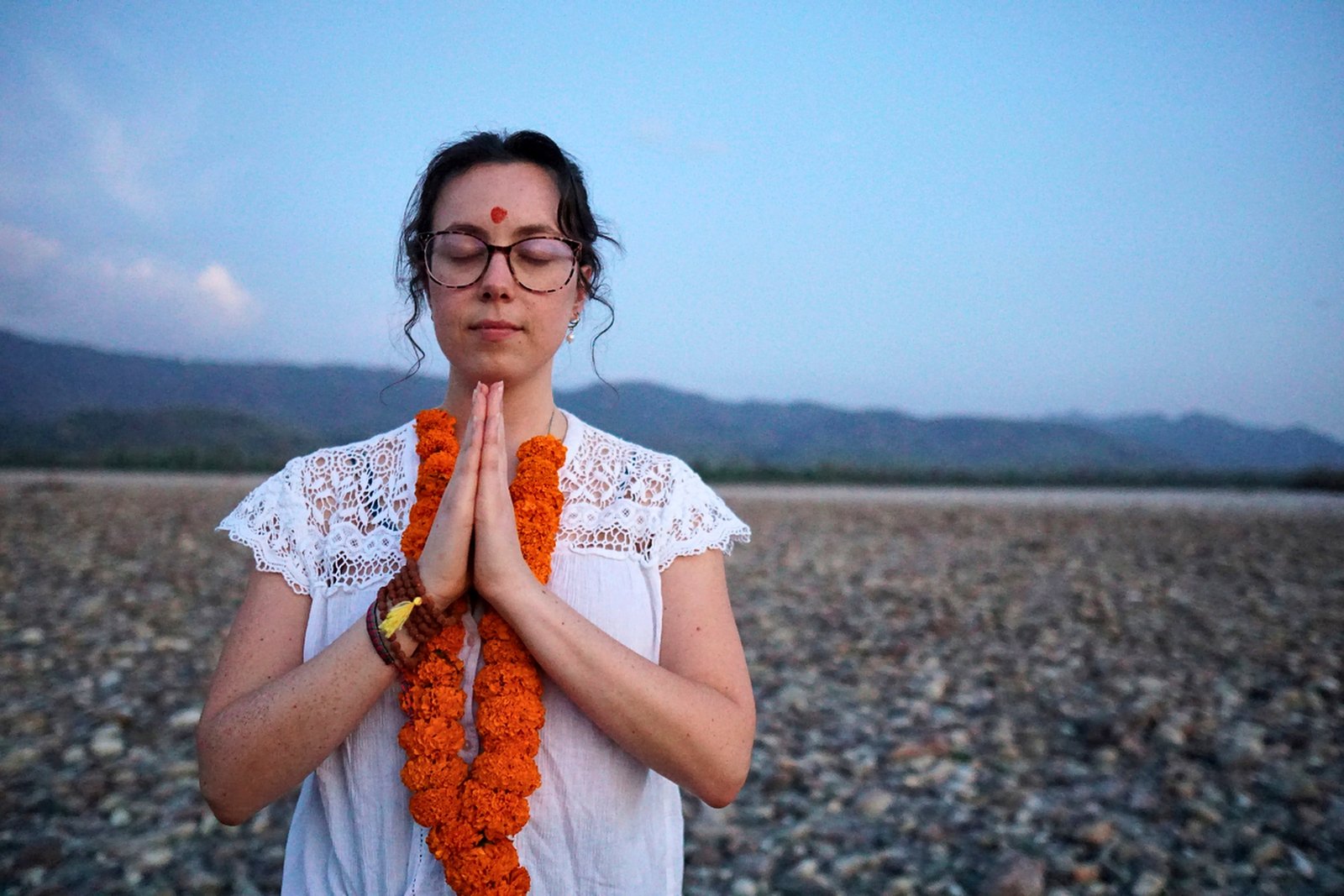Student in a namaste meditation pose by the Ganga during a 7-day retreat in Rishikesh