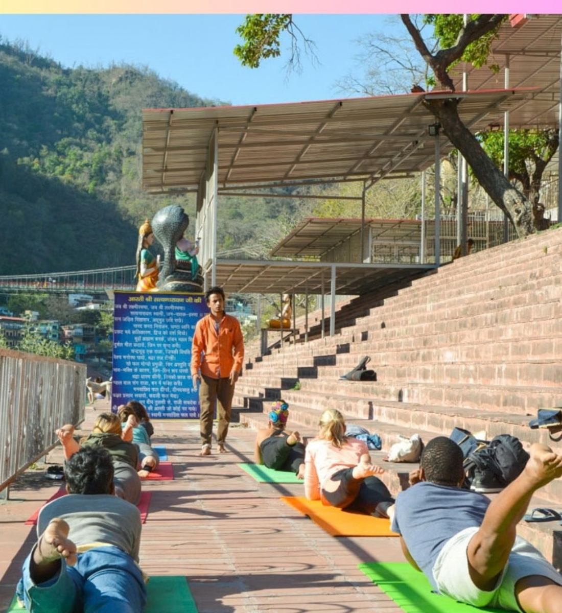 Complete beginner receiving hands-on guidance during an outdoor yoga class on the Ganga ghat in Rishikesh