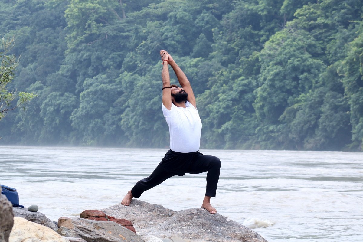Person practicing a yoga pose Warrior 1 (Virabhadrasana I) in the morning near Ganga Banks