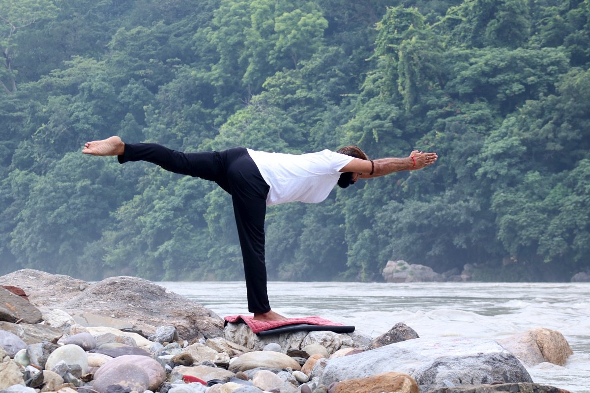 Warrior 3 pose on the rocks beside the Ganga river in Rishikesh